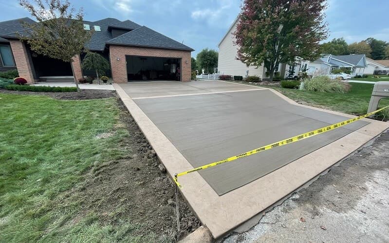 Freshly poured concrete driveway with a contrasting border, caution tape still up
