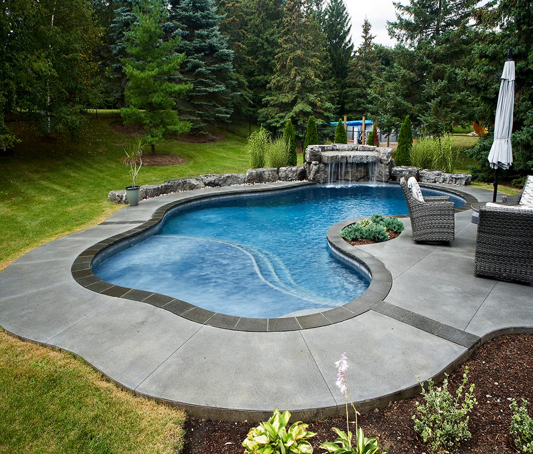 Freeform backyard pool with a stamped concrete deck and stone waterfall